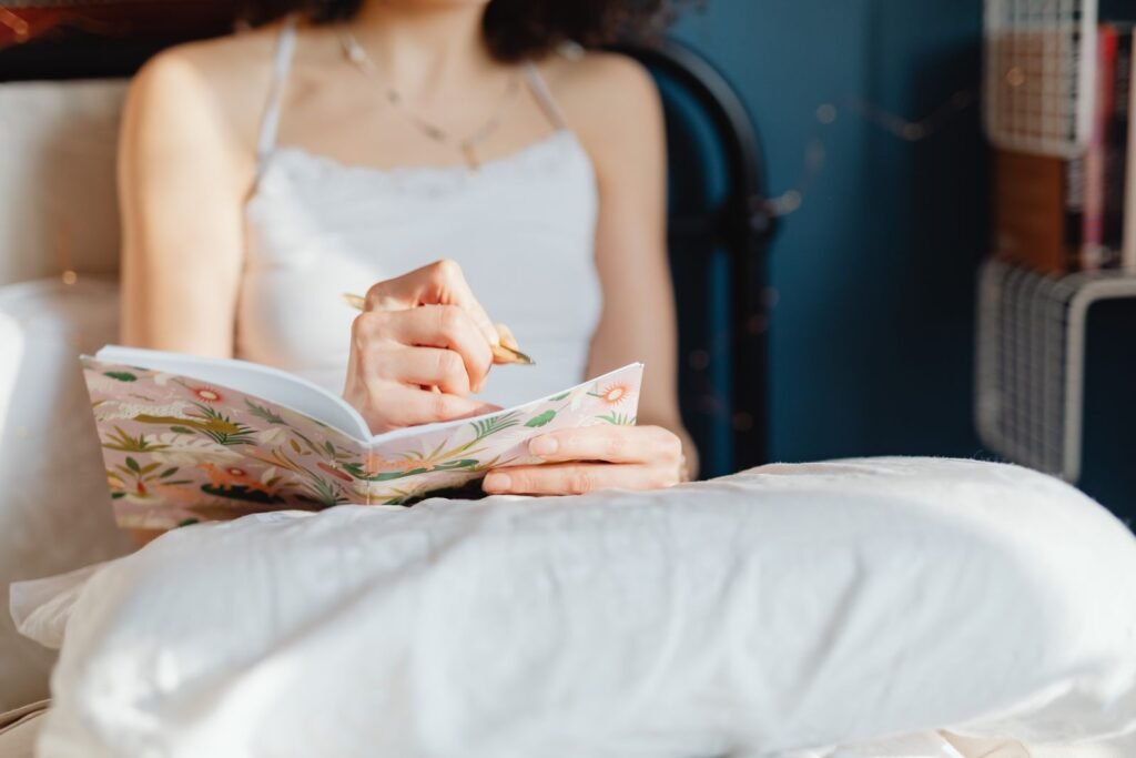 Femme assise sur son lit qui écrit dans un carnet fleuri