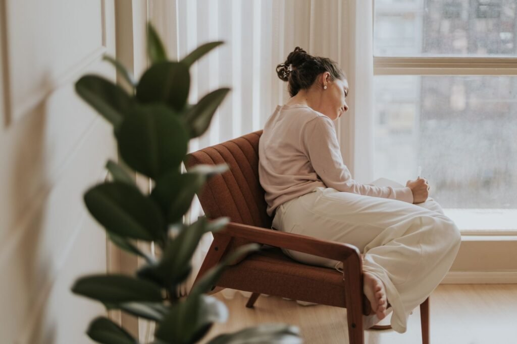 Femme assise dans un fauteuil près d'une fenêtre, pensive